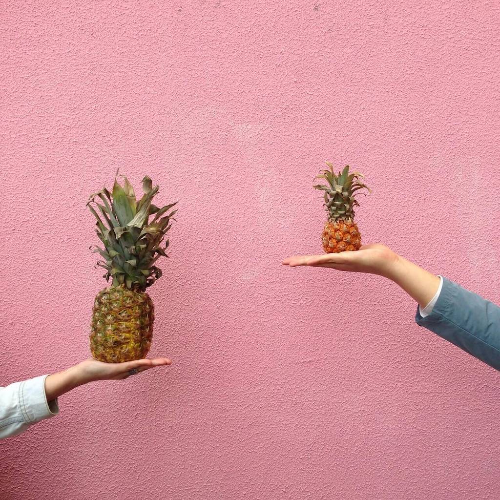 two hands holding up 2 pineapples, one significantly larger than the other